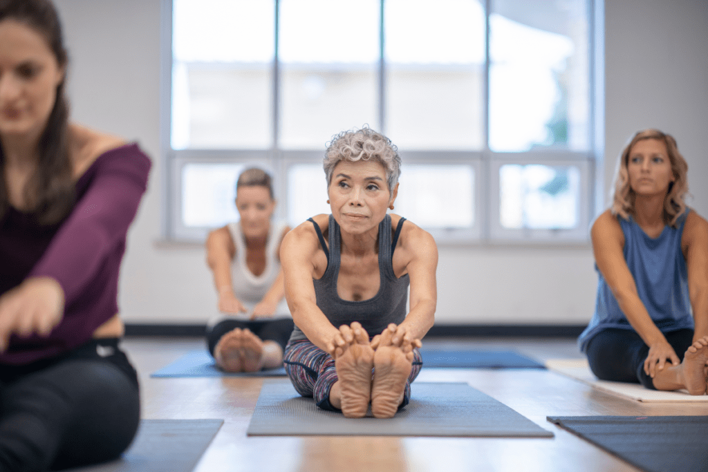 um grupo de adultos sentados em tapetes de yoga tocando os dedos dos pes